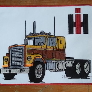 May include: A yellow and brown embroidered patch of a semi-truck with the IH logo in red and black. The truck has a large grill and a single cab.