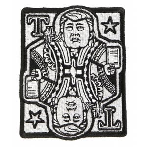 Puede incluir: Parche bordado en blanco y negro que representa una carta de juego con un retrato. El diseño de la carta incluye las letras "T" y "J" y formas de estrella. El parche tiene un borde negro.