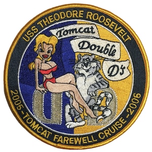 May include: A circular embroidered patch with a gold border and black background. The patch features a cartoon woman in a red bikini, a cartoon cat, and the text "USS Theodore Roosevelt Tomcat Double D's 2005-Tomcat Farewell Cruise-2006".