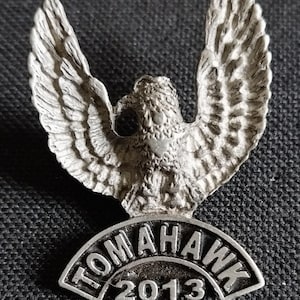 May include: Silver metal pin with a hawk design and the text "Tomahawk 2013" underneath.