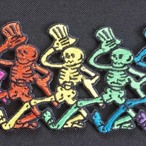 May include: Seven skeleton figures in a line, each wearing a top hat and dancing. The skeletons are rainbow colored, starting with pink, orange, yellow, green, blue, purple, and ending with a dark purple.