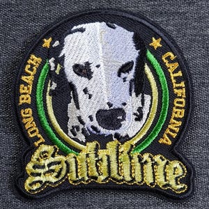 May include: Embroidered patch featuring a dalmatian dog design. The patch is circular with the words "LONG BEACH CALIFORNIA" and "Sublime" in gold lettering. The dog's face is white with black spots, set against a black background.