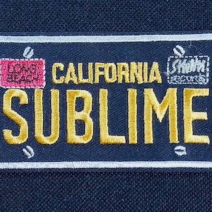 May include: Embroidered patch in the shape of a California license plate. The patch is navy blue with white trim and features the word "SUBIME" in yellow, along with "CALIFORNIA", "LONG BEACH", and "Skunk Records".