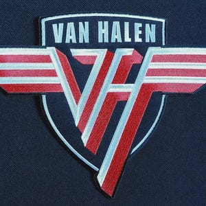 Puede incluir: Parche bordado con el nombre de la banda "VAN HALEN" en letras plateadas sobre un logotipo "VH" estilizado. El logotipo incorpora alas a rayas rojas y blancas, sobre un fondo azul marino.