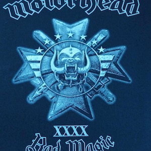 May include: A blue and white graphic of a skull with horns and a starburst design. The text "Motörhead" is at the top of the image and "XXXX Bad Magic" is at the bottom. The text "©2015 Motorhead. Under license to Global Merchandising Services Ltd." is at the bottom of the image.