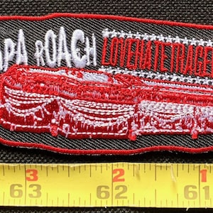 Puede incluir: Un parche bordado rojo y blanco con el texto "Papa Roach Lovers Hate Tragedy" y un ataúd rojo con ribetes blancos.