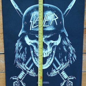 May include: Black patch featuring a skull wearing a helmet with the word "SLAYER" in white. Two crossed swords are behind the skull. The patch is approximately 14 inches long.