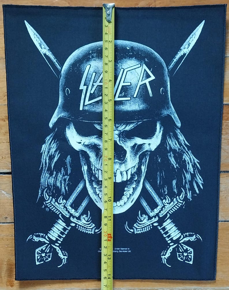 May include: Black patch featuring a skull wearing a helmet with the word "SLAYER" in white. Two crossed swords are behind the skull. The patch is approximately 14 inches long.