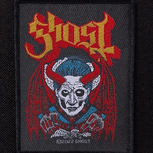 Puede incluir: Parche bordado con la palabra "GHOST" en letras rojas y doradas sobre una ilustración detallada de una figura demoníaca con cuernos y alas rojas. La figura tiene pelo azul y una cara blanca. El parche está bordeado en negro e incluye el texto "©2022 GHOST".