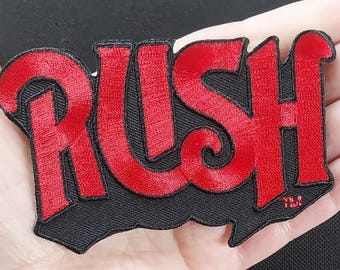 Könnte beinhalten: Roter gestickter Aufnäher mit dem Wort "RUSH" in einer stilisierten Schriftart auf schwarzem Hintergrund.