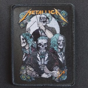 May include: A rectangular embroidered patch featuring the Metallica logo in gold thread at the top. The design depicts four skeleton figures in formal attire, including one conducting with a baton, set against a white circular background.
