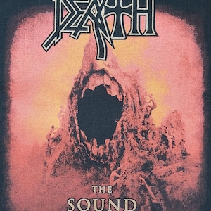 May include: Black t-shirt featuring the band name "DEATH" in a white, stylized font above a graphic of a skull-like rock formation. The text "THE SOUND OF PERSEVERANCE" is below the graphic.