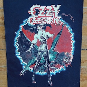Puede incluir: Parche rectangular negro con el nombre "OZZY OSBOURNE" en rojo y blanco. El gráfico muestra una figura con top blanco y pantalón plateado, con un monstruo sobre un fondo rojo y verde.