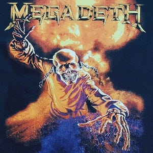 May include: Black t-shirt featuring the band name "MEGADETH" in a metallic, spiky font above a skeletal figure engulfed in flames. The figure is reaching out with bony hands against a fiery explosion background.