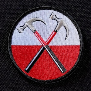 May include: Embroidered patch featuring a circular design with a white and red background. Two crossed silver claw hammers with red handles and black shafts are centered on the patch. The patch has a black border.