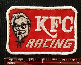 May include: A red and white embroidered patch with the text "KFC Racing" and a cartoon image of Colonel Sanders.