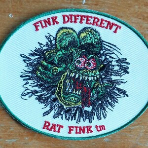 Peut inclure: Un écusson brodé blanc avec un monstre vert, noir et rouge avec le texte "Fink Different" et "Rat Fink tm" en vert.