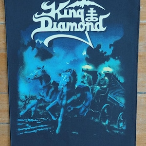 May include: A rectangular patch featuring the band King Diamond. The design depicts a horse-drawn carriage with riders, rendered in shades of blue and white against a dark blue background. The band's logo is at the top.