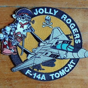 May include: Embroidered patch with a cartoon cat in a pirate hat and attire, smoking a pipe, and an F-14A Tomcat jet. The patch has the words "JOLLY ROGERS" and "F-14A TOMCAT" in white lettering, with a skull and crossbones.