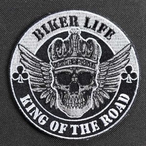 Puede incluir: Parche bordado en blanco y negro con una calavera con una corona y alas. El texto "Biker Life King of the Road" rodea la calavera.