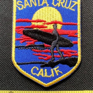May include: A blue and gold embroidered patch with the text "SANTA CRUZ CALIF." and a silhouette of a surfer riding a wave at sunset.
