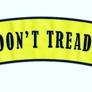 May include: A yellow curved patch with a black border. The patch features a coiled rattlesnake with a green background and the text "DON'T TREAD ON ME" in black.