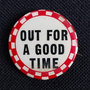 May include: A round button with the text "OUT FOR A GOOD TIME" in black letters on a white background. The button has a red and white checkered border and a pin on the back.
