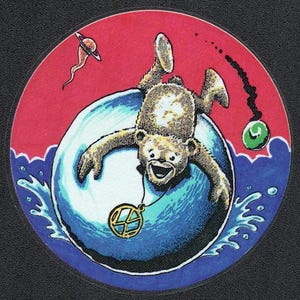 May include: A circular sticker featuring a brown bear diving into a large blue sphere of water. The bear wears a gold peace sign necklace. The background is red with a small planet and a green orb with a black trail. Blue water splashes below.