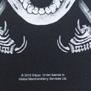 May include: Black fabric with a white, detailed illustration of a skull's open mouth and teeth. The text "&copy; 2016 Slayer. Under license to Global Merchandising Services Ltd." is printed in white.