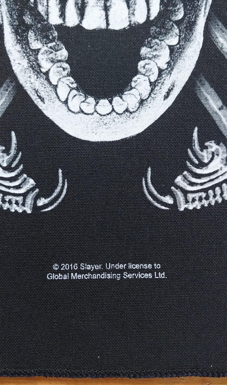 May include: Black fabric with a white, detailed illustration of a skull's open mouth and teeth. The text "&copy; 2016 Slayer. Under license to Global Merchandising Services Ltd." is printed in white.