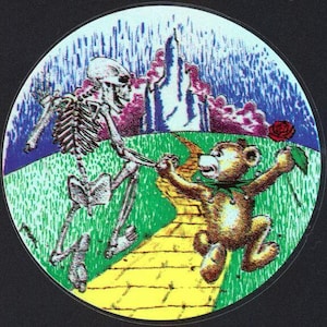 May include: A circular patch featuring a white skeleton and a brown teddy bear holding hands while walking along a yellow brick road. The background includes a green grassy field and a blue sky with purple clouds. The bear holds a single red rose.