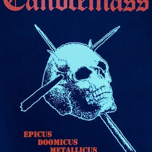 May include: Dark blue t-shirt featuring the word "Candlemass" in red gothic lettering. A light blue skull with crossed spears is centered below the text. The words "EPICUS DOOMICUS METALLICUS" are printed in red.