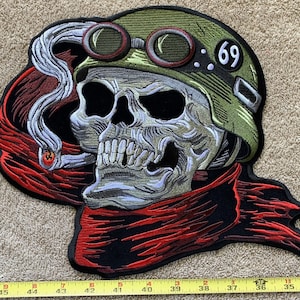 May include: A black and red embroidered patch of a skull wearing a green helmet with goggles and a cigarette in its mouth. The helmet has the number 69 on it.