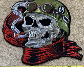May include: A black and red embroidered patch of a skull wearing a green helmet with goggles and a cigarette in its mouth. The helmet has the number 69 on it.
