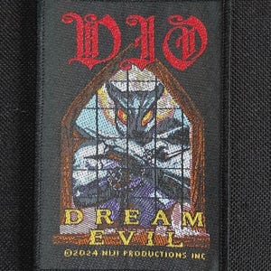 May include: A rectangular embroidered patch featuring the red text DIO at the top. Below is a stained glass window design with a dark creature, the yellow text DREAM EVIL, and the white text 2024 Niji Productions Inc at the bottom.