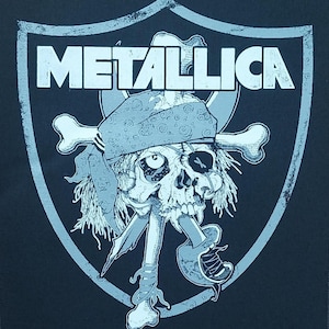 Könnte beinhalten: Schwarze Grafik mit dem Bandnamen "METALLICA" über einem Totenkopf- und gekreuzten Knochen-Design. Der Schädel trägt ein Bandana und hat eine Piraten-Ästhetik, vor einem schildförmigen Hintergrund. Das Design ist in Grau- und Weißtönen gehalten.