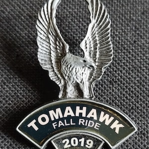 May include: A silver eagle with outstretched wings, perched atop a black and silver Tomahawk Fall Ride 2019 patch.