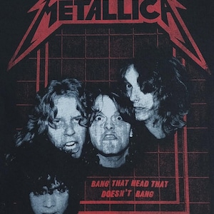 May include: Black t-shirt featuring the band Metallica with a red logo and band members' faces. The text "BANG THAT HEAD THAT DOESN'T BANG" is printed in red. Copyright 2017 Metallica.