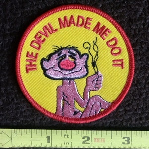 Könnte beinhalten: Ein gestickter Aufnäher in Gelb und Rot mit einer Comicfigur und dem Text "The Devil Made Me Do It".