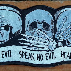 May include: A black and white embroidered patch with three skull faces. The skulls are covering their eyes, mouth, and ears with their hands. The text "See No Evil Speak No Evil Hear No Evil" is written below the skulls.