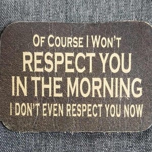 Op de afbeelding: Een bruin leren patch met witte tekst die luidt: "Natuurlijk zal ik je 's morgens niet respecteren. Ik respecteer je nu zelfs niet."