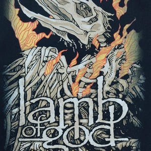 May include: Black graphic featuring a skeletal bird-like figure with flames and the words "Lamb of God" in a stylized font. The design includes additional symbols and text at the bottom, with a dark background.
