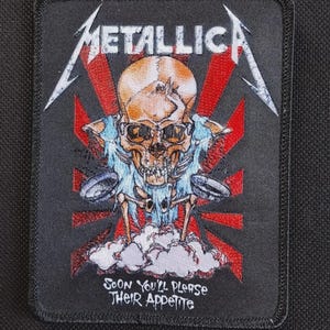 May include: A rectangular black embroidered patch featuring the Metallica logo in white at the top. The center shows a skull with light blue fabric, red sunburst rays, and white clouds. The text reads: SOON YOU'LL PLEASE THEIR APPETITE.