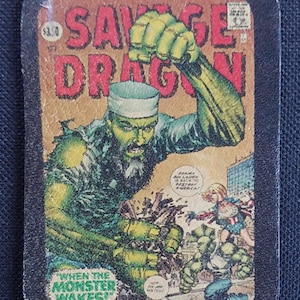 May include: A vintage comic book cover featuring a green, monstrous figure with a beard and a white hat. The comic book is titled "Savage Dragon" and has the text "When the Monster Wakes!" on the bottom. The cover also features a woman in a red, white, and blue costume.