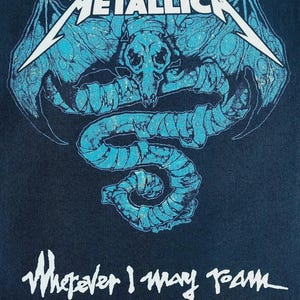 Könnte beinhalten: Dunkelblaues T-Shirt mit dem weißen Schriftzug "METALLICA" über einer türkisfarbenen Grafik eines Schädels und Schlangenmotivs. Der Text "Wherever I May Roam" befindet sich darunter. Copyright-Informationen unten.