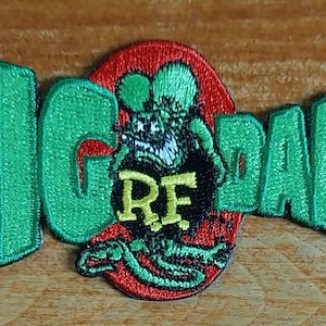 Puede incluir: Parche bordado verde con las palabras "BIG DADDY" y un monstruo de dibujos animados con las letras "RF" en el pecho. El monstruo es verde, negro y rojo.