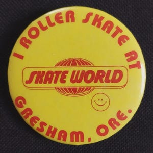 May include: A round yellow pinback button featuring red text that reads I ROLLER SKATE AT SKATE WORLD GRESHAM, ORE. The center includes a red graphic of a globe with a horizontal bar and a small red smiley face icon located in the lower right area.
