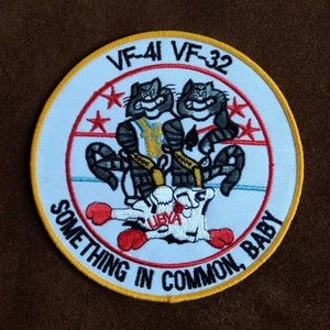 Op de afbeelding: Een witte geborduurde patch met een gele rand. Het bevat twee cartoonkatten met bokshandschoenen en de tekst "VF-41 VF-32 Something in Common Baby".