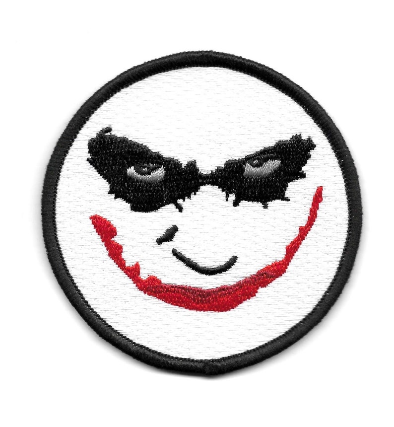 Peut inclure: Un &eacute;cusson brod&eacute; blanc avec un contour noir, repr&eacute;sentant un visage de type Joker avec un sourire rouge et des yeux noirs.