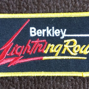 May include: A black rectangular patch with a yellow border. The patch has a red and yellow lightning bolt design with the text "Berkley Lightning Rod" in white and gold lettering.